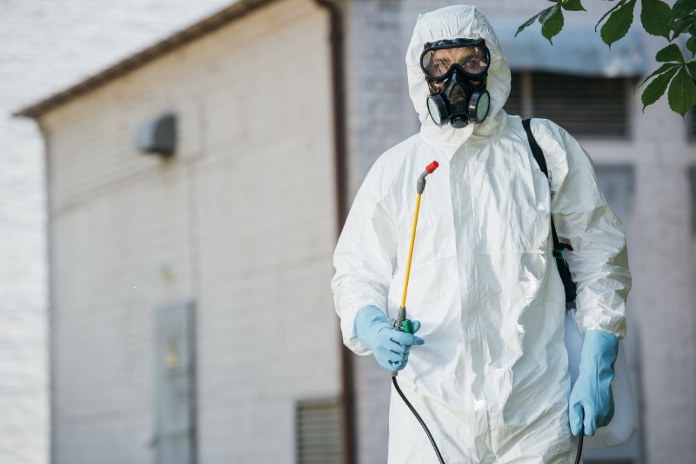 A man in a protective suit and mask applies spray to a house, representing stinging control services in Houston, TX.